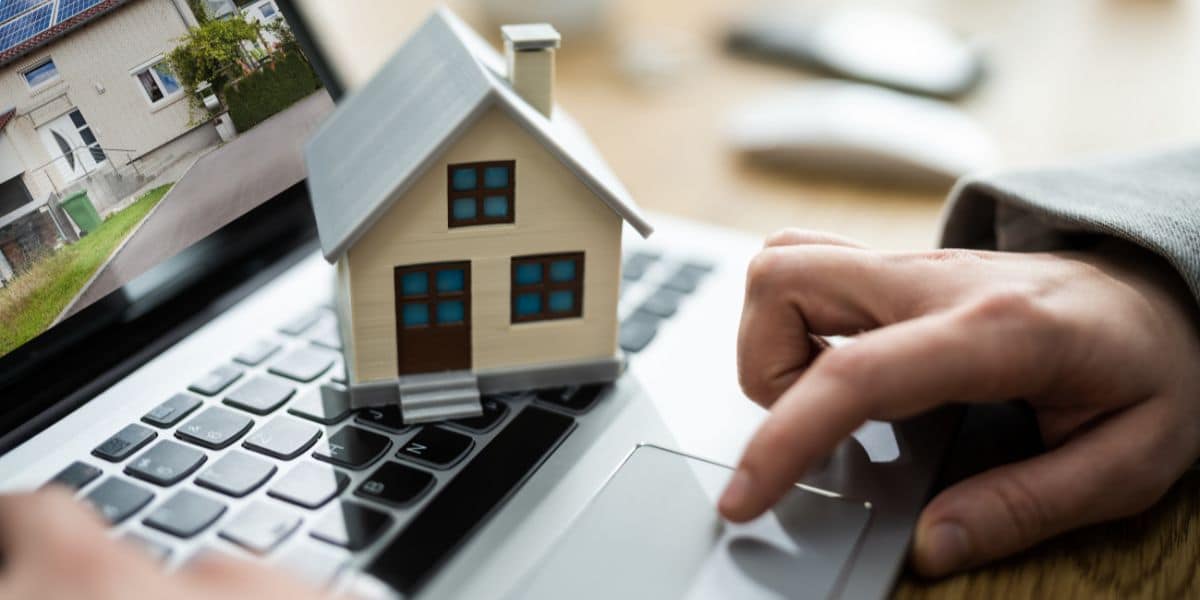 Person using a laptop with a small model house placed on the keyboard.